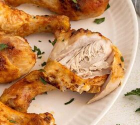 air fryer chicken legs crispy juicy and easy, Four cooked chicken drumsticks on a white plate garnished with chopped parsley One drumstick is cut open showing tender juicy white meat inside A few parsley leaves are scattered on the table nearby