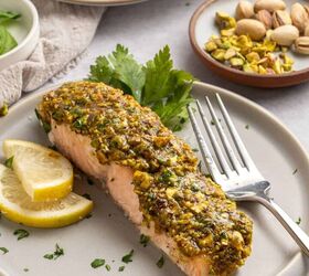 pistachio crusted salmon with lemon and za atar, A plate with a slice of pistachio crusted salmon topped with a vibrant green pistachio crust and garnished with lemon slices and parsley A fork rests on the plate with a dish of pistachios in the background