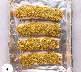 pistachio crusted salmon with lemon and za atar, Four pistachio crusted salmon fillets are coated in a crushed pistachio crust and arranged on a foil lined baking sheet The image is shot from above on a light background with a small white circle labeled 4 in the bottom left corner