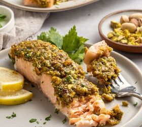pistachio crusted salmon with lemon and za atar, A fork holds a bite of pistachio crusted salmon a fillet topped with a chopped pistachio crust served with lemon slices and parsley In the background more pistachios and another plate of fish complete the scene