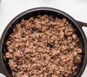 nacho fries with ground beef easy 30 minute recipe, A black skillet filled with cooked ground beef sits on a white surface surrounded by a bowl of chopped green onions a whole tomato and a green jalape o pepper