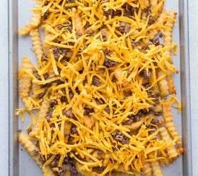 nacho fries with ground beef easy 30 minute recipe, A baking tray filled with crinkle cut French fries topped with ground beef and shredded cheddar cheese ready to be baked