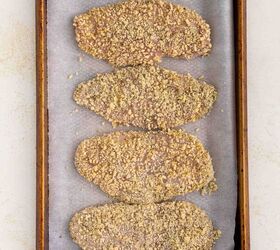 baked parmesan crusted chicken better than fried, Four breaded cutlets are arranged in a single layer on a parchment lined baking sheet ready to be baked The cutlets are evenly coated with a crumb mixture