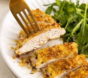 baked parmesan crusted chicken better than fried, A close up of a breaded and baked chicken cutlet sliced on a white plate with a fork holding one piece Fresh green arugula is served on the side