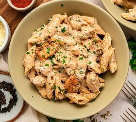 garlic parmesan pasta with chicken, A bowl of creamy garlic parmesan pasta with chicken topped with tender grilled pieces is sprinkled with chopped parsley and parmesan cheese Surrounding the bowl are peppercorns grated cheese forks and a small bowl of paprika