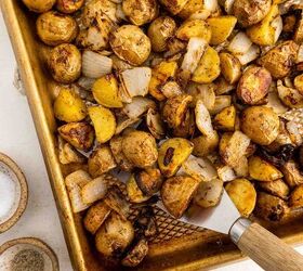 crispy roasted potatoes and onions, A baking sheet filled with roasted baby potatoes and chopped onions seasoned and golden brown with a spatula lifting a portion Plates and small bowls are nearby