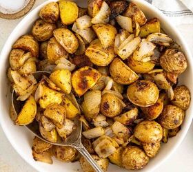 crispy roasted potatoes and onions, A white bowl filled with roasted potatoes and onions seasoned with herbs sits on a light surface with a serving spoon Salt pepper and a striped napkin are nearby