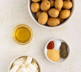 crispy roasted potatoes and onions, A bowl of small potatoes a bowl of chopped onions a small bowl with olive oil and a small bowl containing salt pepper paprika garlic powder and dried herbs are arranged on a light colored surface