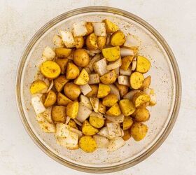 crispy roasted potatoes and onions, A clear glass bowl filled with diced yellow potatoes and white onions coated with spices sits on a light colored surface