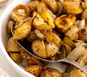 crispy roasted potatoes and onions, A close up of roasted potatoes and onions in a white bowl with a spoon scooping up some of the golden brown seasoned potato pieces