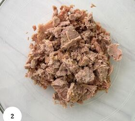 mediterranean chickpea tuna salad no mayo, A clear glass bowl containing flaked light brown canned tuna for a chickpea tuna salad is placed on a white surface A white circle with the number 2 is in the lower left corner of the image
