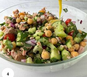 mediterranean chickpea tuna salad no mayo, A glass bowl filled with a vibrant chickpea tuna salad tuna chickpeas cucumber tomatoes red onion and parsley all brought together as yellow dressing is poured over the fresh ingredients