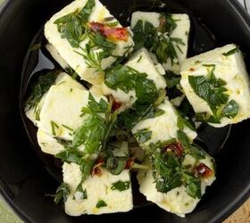 greek yogurt french onion dip with real caramelized onions, A black bowl filled with cubes of marinated feta cheese in herbs and oil garnished with chopped parsley and red pepper Slices of bread a spoon and a green napkin are nearby on a white surface