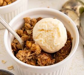 air fryer apple crisp, A white ramekin filled with apple crisp topped with a scoop of vanilla ice cream and a spoon Crumbled oats and another ramekin are visible nearby