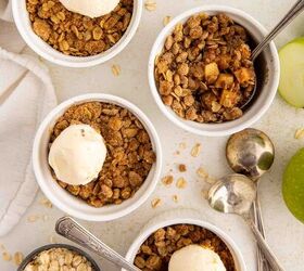 air fryer apple crisp, Four ramekins of apple crisp topped with vanilla ice cream surrounded by oats green apple slices cinnamon sticks and three spoons on a white surface