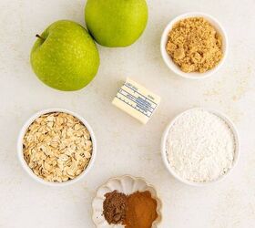 air fryer apple crisp, Two green apples a pat of butter a small bowl of brown sugar a bowl of oats a bowl of flour and a dish with cinnamon and nutmeg are arranged on a light colored surface