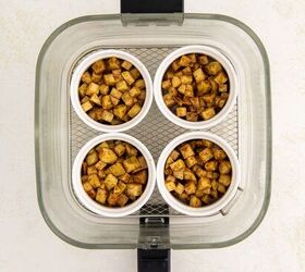 air fryer apple crisp, Top view of four small white ramekins filled with spiced apple cubes arranged in a glass air fryer basket on a light colored surface