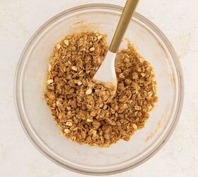 air fryer apple crisp, A glass bowl with crumbly oat mixture and a spoon viewed from above on a light surface