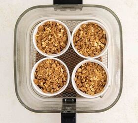 air fryer apple crisp, Four small ramekins filled with crumbly oat topping and apples are arranged in a square inside an air fryer basket viewed from above on a light background