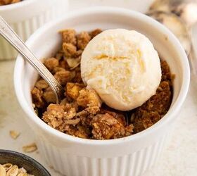 air fryer apple crisp, A white ramekin filled with apple crisp topped with a scoop of vanilla ice cream A spoon rests in the dish and there are apples oats and spoons nearby