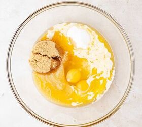 moist applesauce muffins, A glass mixing bowl containing brown sugar two eggs melted butter and flour on a light colored countertop viewed from above