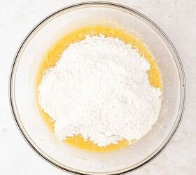 moist applesauce muffins, A glass mixing bowl with flour sitting on top of a yellow liquid mixture placed on a light colored marble surface