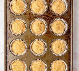 moist applesauce muffins, A metal muffin tin holds twelve cupcake liners filled with unbaked batter each topped with a crumbly streusel ready to be baked The tin rests on a light colored surface