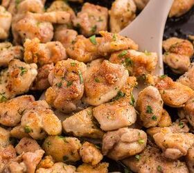garlic butter chicken bites ready in 20 minutes, Golden brown seasoned chicken pieces being saut ed in a pan with a spatula garnished with chopped herbs