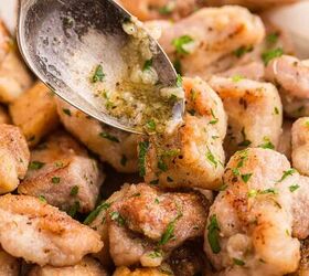 garlic butter chicken bites ready in 20 minutes, A spoon drizzles garlic butter sauce over golden pan seared pieces of chicken garnished with chopped parsley on a white plate
