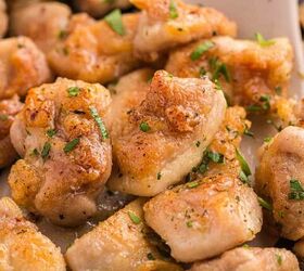 garlic butter chicken bites ready in 20 minutes, Close up of golden brown pan seared chicken pieces garnished with chopped parsley served on a beige spatula