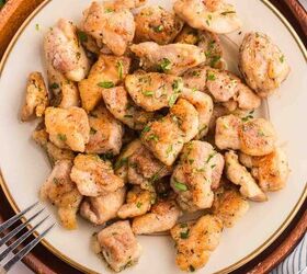 garlic butter chicken bites ready in 20 minutes, A plate of cooked golden brown chicken bites garnished with chopped herbs set on a round wooden tray with a fork nearby