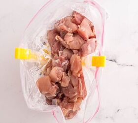 garlic butter chicken bites ready in 20 minutes, Raw diced chicken placed inside a clear plastic zip top bag that is held open with yellow bag holders set on a white marble surface