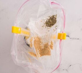 garlic butter chicken bites ready in 20 minutes, A plastic zip top bag held open with clips contains various spices and seasonings including brown and green powders on a light marble surface