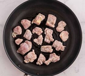 garlic butter chicken bites ready in 20 minutes, Raw seasoned pieces of chicken are spread out in a single layer in a black nonstick frying pan with a silver handle ready to be cooked The pan is placed on a light colored marbled surface