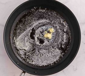 garlic butter chicken bites ready in 20 minutes, A black frying pan with melted butter and a small amount of minced garlic cooking on a marble countertop