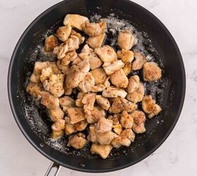garlic butter chicken bites ready in 20 minutes, A black frying pan filled with cooked seasoned pieces of chicken sits on a white marble surface