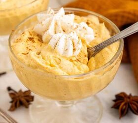 creamy pumpkin mousse easy no bake, A glass bowl filled with creamy pumpkin mousse topped with whipped cream and a sprinkle of cinnamon with a spoon inside Star anise and cloves are nearby on the table
